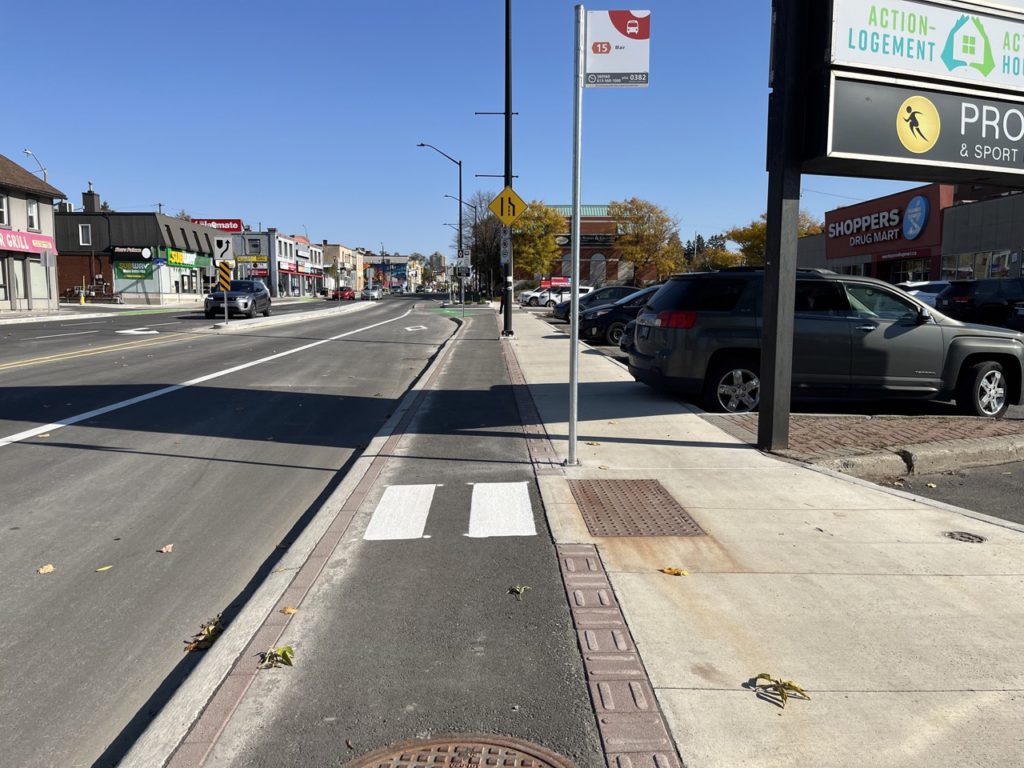 Cycle track runs down the middle of the picture, and we see an OC transpo bus stop sign. 