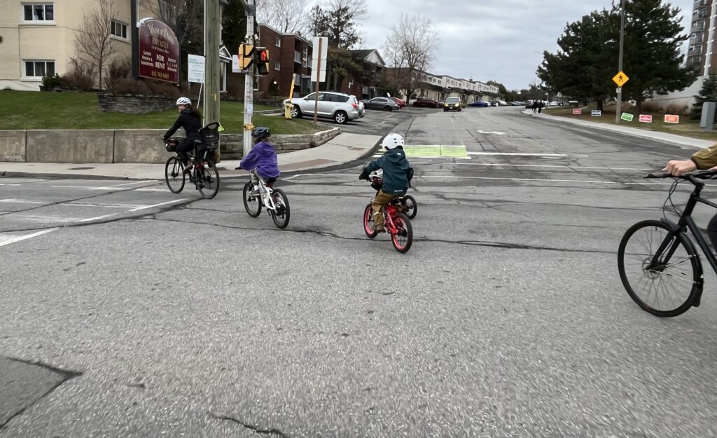 One adult and two kids on bikes turning left on a main street.