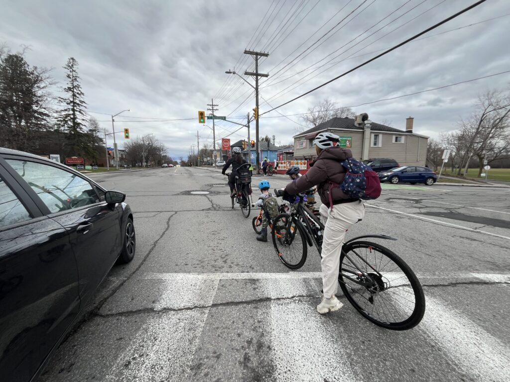 Bike bus crew starting to turn left onto Hemlock. There’s a car to their left at a safe enough distance. To their right, in the background, one can see a green bike box on the adjacent street.