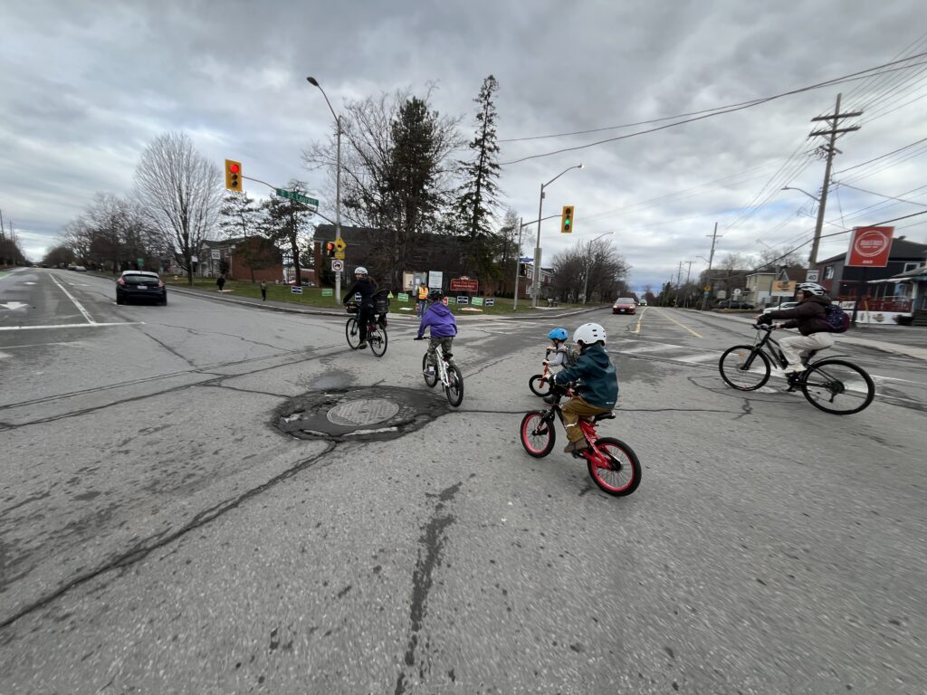 Bike bus crew turning left. One adult is leading, another adult protecting them on the outside and photographer is shielding on the inside of the group.