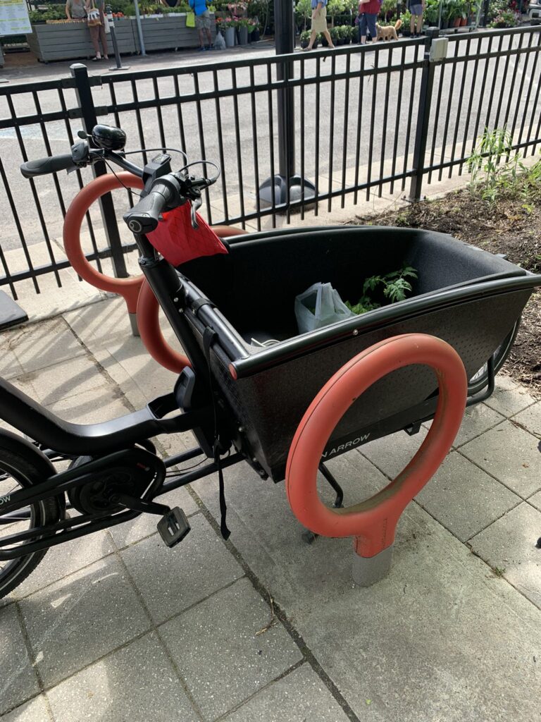 Picture of two front loading cargo bicycles parked and locked at staple style locks. 