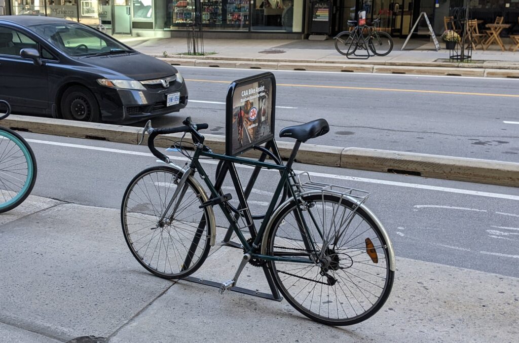 A standard road style bicycle locked to the outside of a coat hanger bicycle rack, as locking to the middle ring is not possible due to the style of bicycle rack.